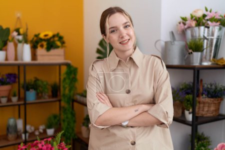 Foto de Joven florista mujer caucásica sonriendo confiado de pie con los brazos cruzados gesto en la tienda de flores - Imagen libre de derechos