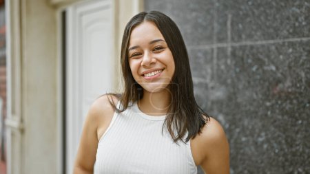 Photo for Smiling young hispanic woman full of joy stands confidently on an urban street, her happy expression capturing her cool, casual lifestyle. this beautiful portrait shows her happiness outdoors. - Royalty Free Image