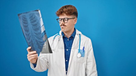 Foto de Joven médico hispano buscando rayos X sobre fondo azul aislado - Imagen libre de derechos
