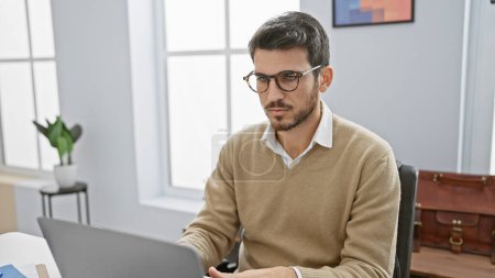 Schöner hispanischer Mann mit Bart arbeitet am Laptop im hellen Büroraum.