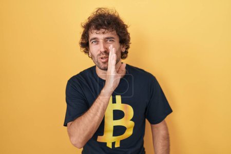 Photo for Hispanic young man wearing bitcoin t shirt hand on mouth telling secret rumor, whispering malicious talk conversation - Royalty Free Image