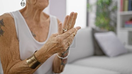 Photo for Senior grey-haired woman suffering intense hand pain, sitting in living room sofa at home, elderly female with short hair looking hurt, osteoarthritis problem indoors. - Royalty Free Image