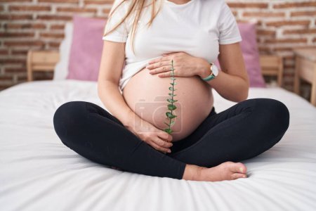 Mujer embarazada joven tocando la planta de retención del vientre en el dormitorio