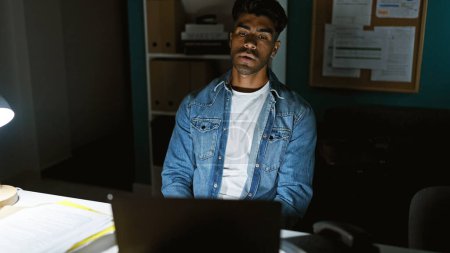 Photo for Handsome hispanic man in office working late on laptop highlighting professionalism in a corporate setting - Royalty Free Image