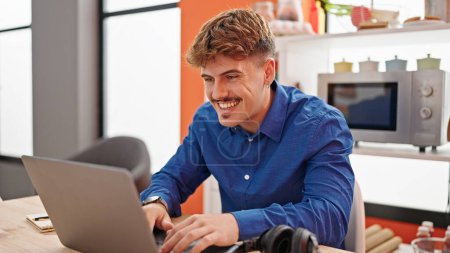 Téléchargez les photos : Jeune homme hispanique utilisant un ordinateur portable assis sur la table souriant à la salle à manger - en image libre de droit