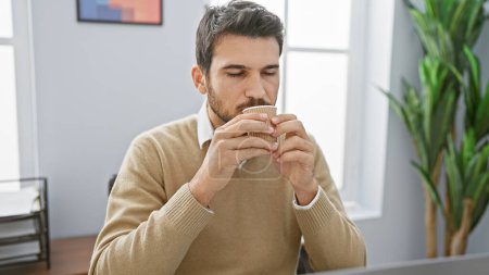 Ein junger hispanischer Mann genießt eine Kaffeepause in einem modernen Büroambiente.