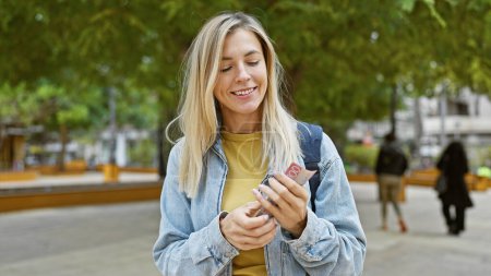 Téléchargez les photos : Une jeune femme caucasienne souriante compte les dollars néo-zélandais à l'extérieur dans un parc verdoyant luxuriant. - en image libre de droit