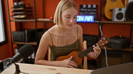 Foto de Joven mujer rubia músico teniendo en línea ukelele lección en el estudio de música - Imagen libre de derechos