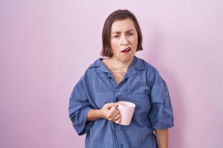 Foto de Mujer hispana de mediana edad bebiendo una taza de café con aspecto somnoliento y cansado, agotado por la fatiga y la resaca, ojos perezosos en la mañana. - Imagen libre de derechos