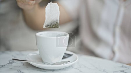 Photo for Young hispanic man putting tea bag on cup at coffee shop terrace - Royalty Free Image