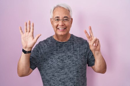 Téléchargez les photos : Homme d'âge moyen avec les cheveux gris debout sur fond rose montrant et pointant vers le haut avec les doigts numéro sept tout en souriant confiant et heureux. - en image libre de droit