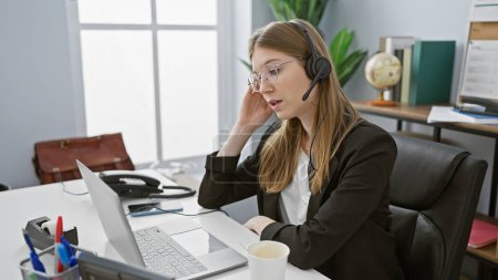 Foto de Una mujer profesional en un auricular que se conecta con un ordenador portátil en un espacio de oficina luminoso - Imagen libre de derechos