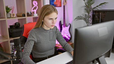 Photo for Blonde woman intensely focusing on her computer screen in a modern gaming room at night. - Royalty Free Image