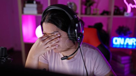 Stressed hispanic woman with headset in neon-lit gaming room at night.