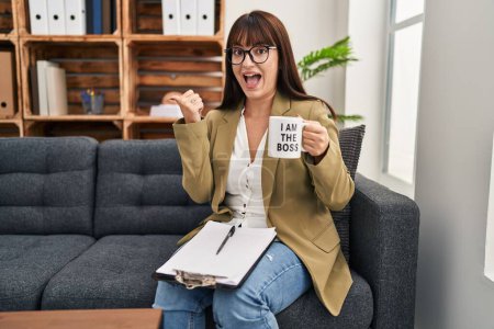 Photo for Young hispanic woman drinking from i am the boss coffee cup pointing thumb up to the side smiling happy with open mouth - Royalty Free Image