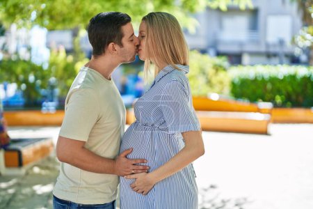 Foto de Hombre y mujer pareja esperando bebé besándose en parque - Imagen libre de derechos