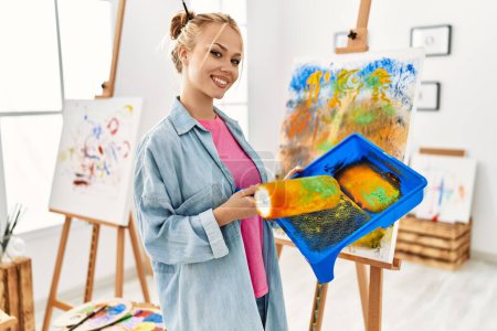 Téléchargez les photos : Jeune artiste femme caucasienne utilisant le dessin au rouleau de peinture au studio d'art - en image libre de droit