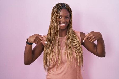 Photo for African american woman with braided hair standing over pink background looking confident with smile on face, pointing oneself with fingers proud and happy. - Royalty Free Image