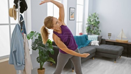 Foto de Mujer madura haciendo ejercicio en una amplia sala de estar, transmitiendo un estilo de vida activo y bienestar en casa. - Imagen libre de derechos