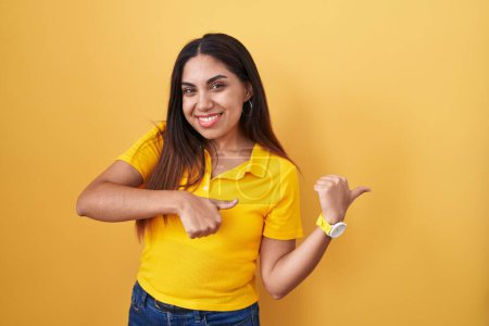 Photo for Young arab woman standing over yellow background pointing to the back behind with hand and thumbs up, smiling confident - Royalty Free Image