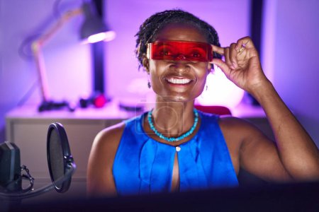 Photo for African woman with dreadlocks playing video games wearing virtual reality glasses looking positive and happy standing and smiling with a confident smile showing teeth - Royalty Free Image