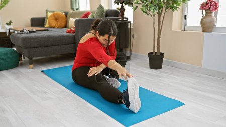 Photo for A smiling woman stretches on a yoga mat at home, depicting a cozy fitness setting in a modern living room. - Royalty Free Image