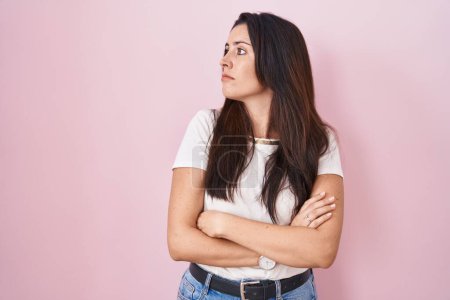 Téléchargez les photos : Jeune femme brune debout sur fond rose regardant sur le côté avec les bras croisés convaincus et confiants - en image libre de droit