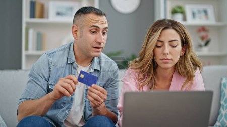 Téléchargez les photos : Homme et femme couple shopping avec ordinateur portable et carte de crédit assis sur le canapé à la maison - en image libre de droit