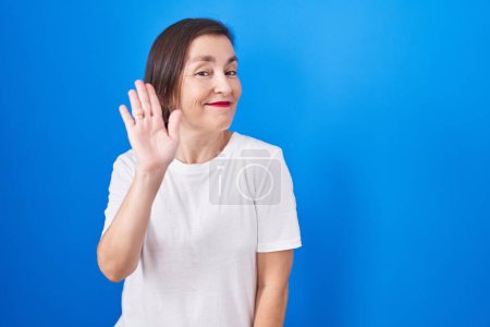 Téléchargez les photos : Middle age hispanic woman standing over blue background waiving saying hello happy and smiling, friendly welcome gesture - en image libre de droit