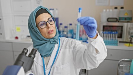 Téléchargez les photos : Une femme scientifique mature en hijab examine une éprouvette en laboratoire. - en image libre de droit