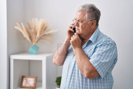Foto de Middle age grey-haired man talking on smartphone standing at home - Imagen libre de derechos