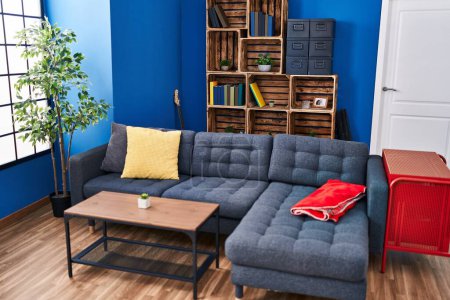 Foto de Una acogedora sala de estar moderna con un sofá seccional azul, estantes de madera, un armario rojo y una planta en maceta junto a una ventana brillante. - Imagen libre de derechos