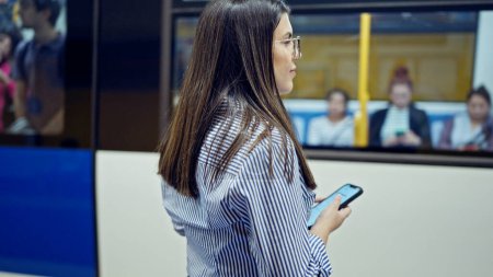 Foto de Joven mujer hispana guapa esperando el metro usando smartphone en la estación de metro de Madrid - Imagen libre de derechos