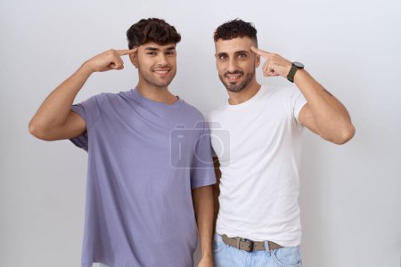 Téléchargez les photos : Couple gay homosexuel debout sur fond blanc souriant pointant vers la tête avec un doigt, grande idée ou pensée, bonne mémoire - en image libre de droit