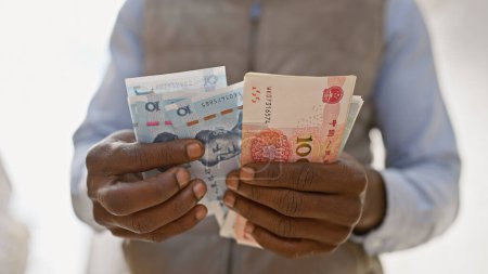 Téléchargez les photos : Homme africain en gilet tenant le yuan chinois et une autre monnaie non identifiable dans une rue urbaine. - en image libre de droit