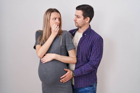 Photo for Young couple expecting a baby standing over white background looking stressed and nervous with hands on mouth biting nails. anxiety problem. - Royalty Free Image