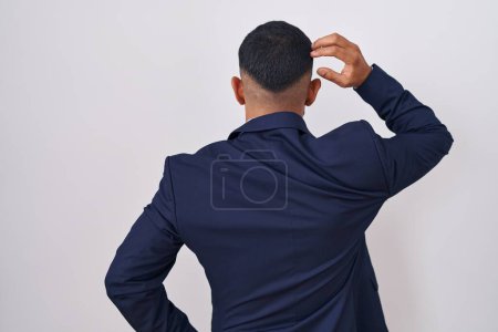 Téléchargez les photos : Jeune homme hispanique portant un costume d'affaires et cravate à l'envers en pensant au doute avec la main sur la tête - en image libre de droit