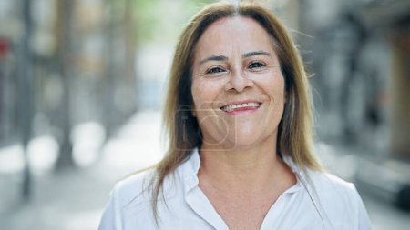 Téléchargez les photos : Moyen Age femme hispanique souriant confiance debout dans la rue - en image libre de droit