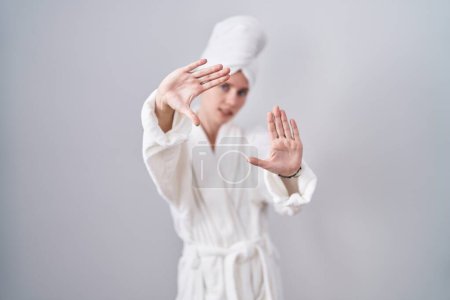 Foto de Mujer rubia caucásica usando albornoz haciendo marco usando las manos palmas y los dedos, perspectiva de la cámara - Imagen libre de derechos