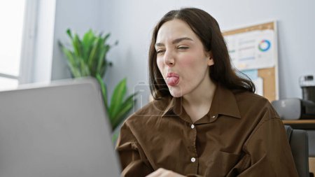 Young caucasian woman making a playful face in a modern office setting, depicting casual workday life.