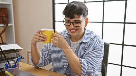Photo for Smiling young man enjoying coffee in a modern office setting, exuding casual professional vibes. - Royalty Free Image