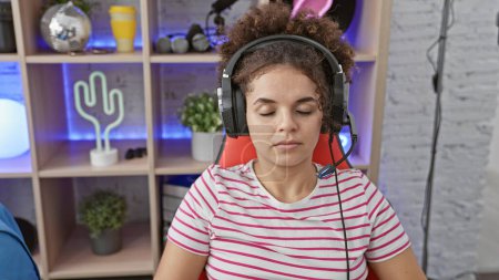 Photo for Hispanic woman with curly hair wearing headset sits peacefully in a vibrant gaming room - Royalty Free Image