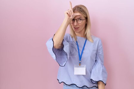 Photo for Young caucasian business woman wearing id card making fun of people with fingers on forehead doing loser gesture mocking and insulting. - Royalty Free Image