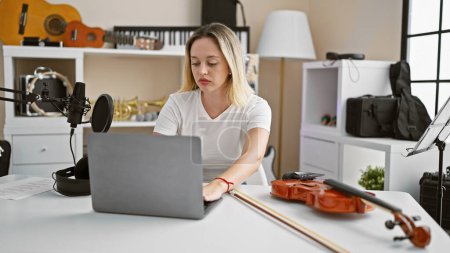 Téléchargez les photos : Jeune musicienne blonde utilisant un ordinateur portable au studio de musique - en image libre de droit