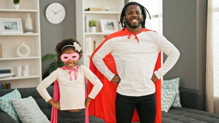 Foto de Padre e hija afroamericanos sonriendo confiados vistiendo traje de superhéroe de pie en casa - Imagen libre de derechos