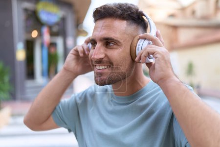 Photo for Young hispanic man listening to music standing at street - Royalty Free Image