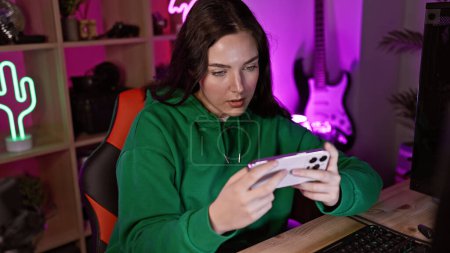 Photo for Focused caucasian woman intently gaming on smartphone in a neon-lit room at night - Royalty Free Image