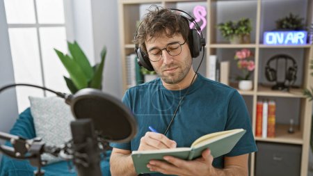 Téléchargez les photos : Un homme concentré avec des écouteurs écrivant des notes dans un studio de radio avec un panneau "on air" allumé en arrière-plan. - en image libre de droit