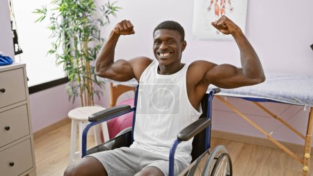 Téléchargez les photos : Bel homme noir fléchissant les muscles avec confiance dans un fauteuil roulant à l'intérieur d'une salle de désintox clinique, représentant la force et la récupération. - en image libre de droit
