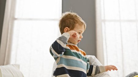 Téléchargez les photos : Tout-petit garçon en chemise rayée regardant fatigué dans la chambre lumineuse - en image libre de droit